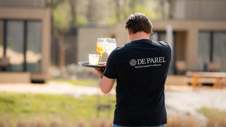 Medewerker in bedrijfskleding brengt drankjes op een dienblad naar het terras