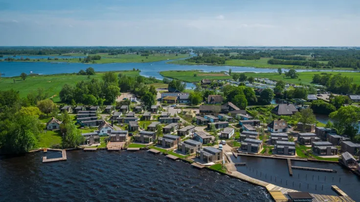 Luchtfoto van het vakantiepark aan het meer met steigers en weilanden erachter