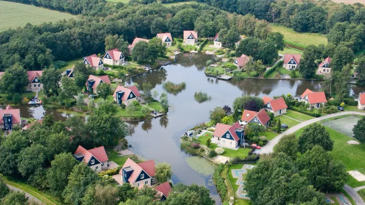 Luchtfoto van het vakantiepark met woningen met rode daken rond een vijver