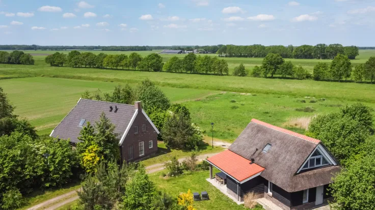 Luchtfoto van twee vakantiewoningen met bomen in het weidse groene landschap