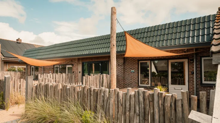 Terras met oranje schaduwdoeken achter een houten hek bij de accommodatie