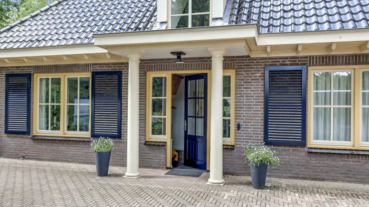 Villa met bakstenen gevel, blauwe luiken, zuilen en een klinkeroprit