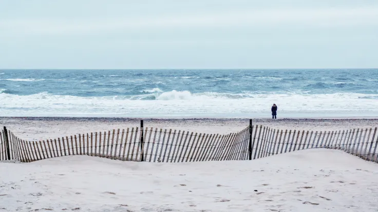 Winters strand met rijshouten schermen en een wandelaar bij de zee
