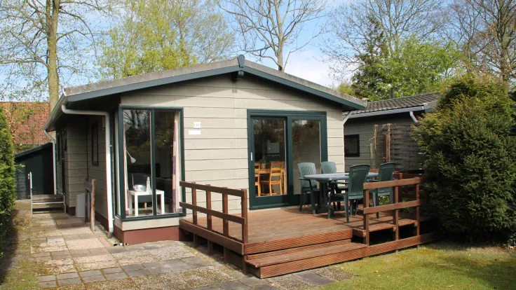 Chalet met houten veranda, groene kozijnen en een terras in de tuin