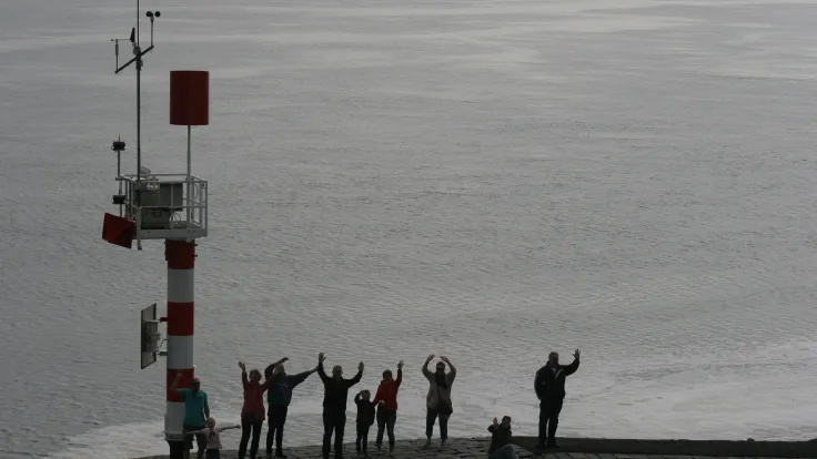 Groep wandelaars met opgestoken armen bij een baken op het wad