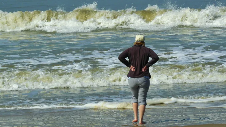 Vrouw staat aan de vloedlijn en kijkt naar de brekende golven