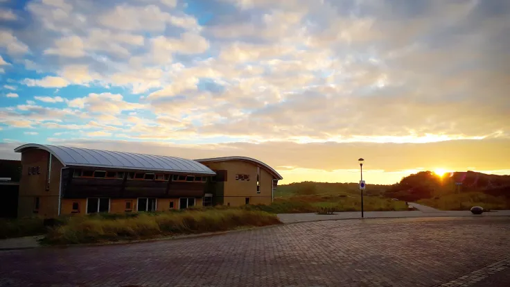 Accommodatiegebouw met parkeerterrein bij zonsondergang in de duinen