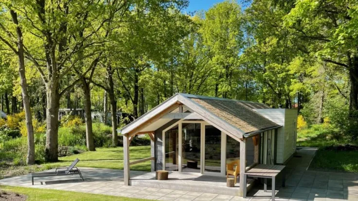 Houten overkapping met glazen wand en een bankje tussen de bomen