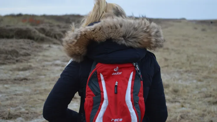 Wandelaarster met rode rugzak kijkt uit over het winterse duinlandschap