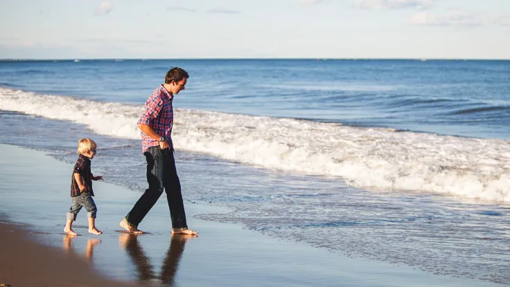 Vader en kind wandelen met blote voeten door de branding op het strand