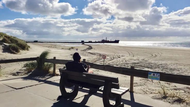 Man zit op een bankje bij de strandopgang met uitzicht over het strand