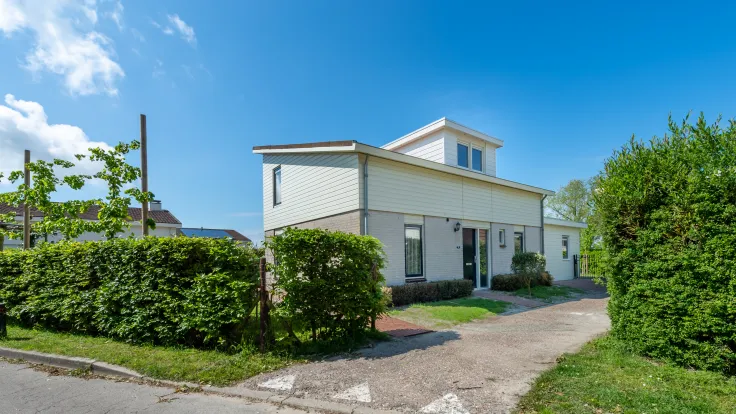 Vakantiewoning met witte gevel en hagen langs de oprit
