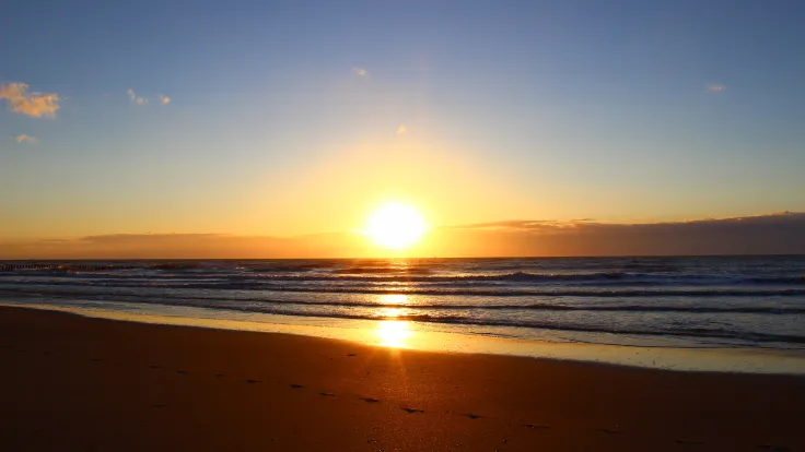 Zonsondergang boven de zee met voetsporen op het lege strand