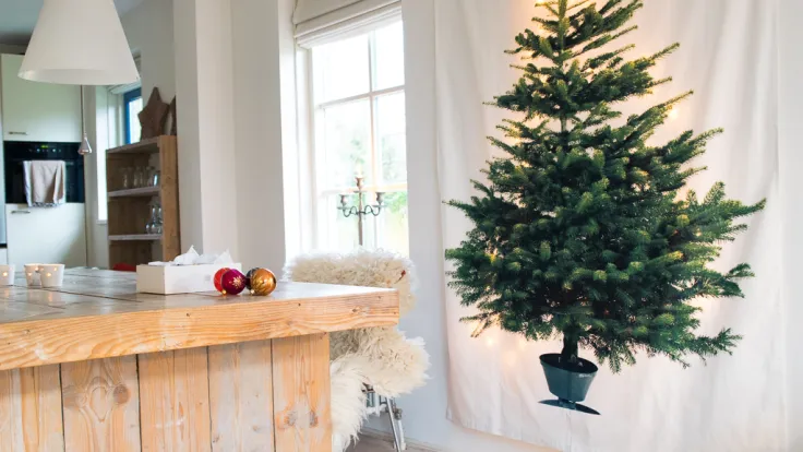 Onversierde kerstboom in een lichte woonkamer met kerstballen op tafel
