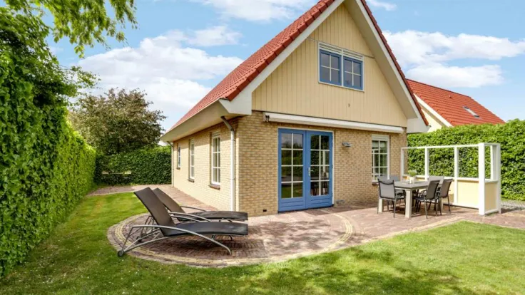 Vakantiewoning met gele gevel, serre en ligbedden op het gazon