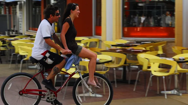 Stel rijdt op een tandem langs een terras met gele stoelen
