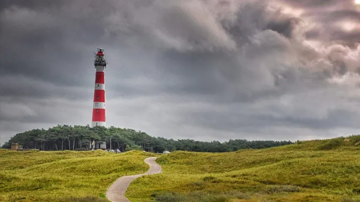 De rood-witte vuurtoren van Ameland boven de duinen onder een dreigende lucht