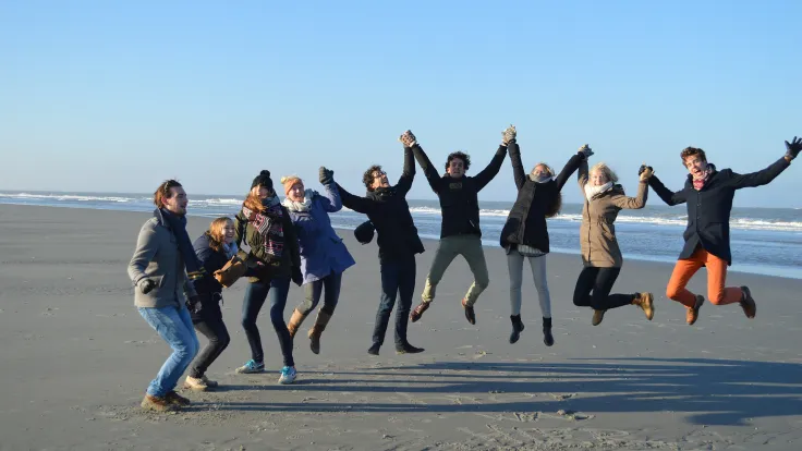 Groep mensen springt hand in hand in de lucht op het strand