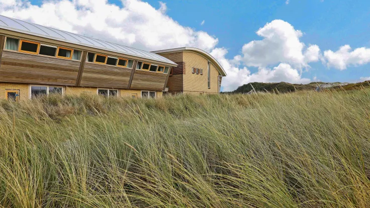 Appartementengebouw met golvend dak achter het helmgras in de duinen