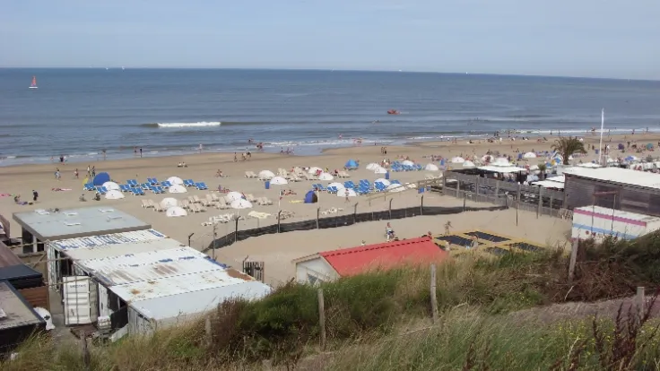 Strandtenten en een druk strand gezien vanaf het duin met de zee erachter